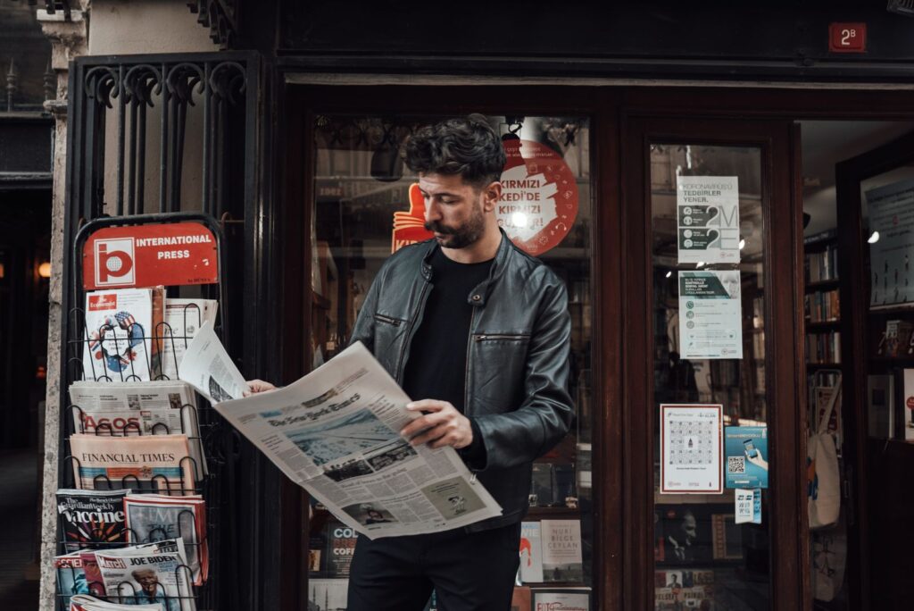 Un hombre lee el periódico junto a un quiosco